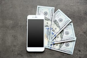 Smart phone with dollar banknotes on grey background. Making money online